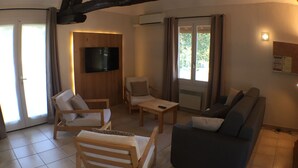 Uma sala de estar com televisão, duas cadeiras, um sofá e uma mesa de centro.