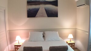 Quarto com cama grande, duas mesas de cabeceira com luminárias, um quadro na parede e vista para um cais.