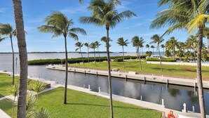 Un paseo marítimo con palmeras, un canal y una vista distante del mar.