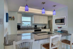 A kitchen with white cabinets, a granite countertop, a built-in microwave, and pendant lights.