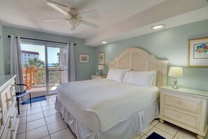 A bedroom with a bed, a nightstand, a chair, a ceiling fan, and a view of the outside.
