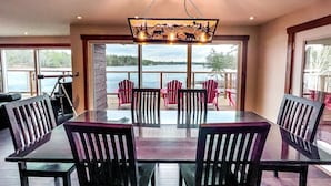 A dining area with a glass table and chairs, large windows with a view of a lake, and a ceiling light fixture. - Muskoka - The Eagle's Nest (Coldwater)