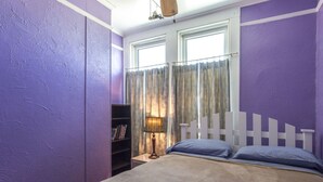 Une chambre à coucher avec un lit, une table de chevet avec une lampe, une bibliothèque et une fenêtre avec des rideaux.
