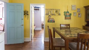 Un coin repas avec une table et des chaises, un mur jaune orné d’ustensiles suspendus et une porte donnant sur une autre pièce.