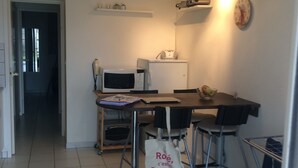 A small kitchen with a microwave, toaster, and a table with chairs. There is a bag on the floor and a clock on the wall. - CAP ESTEREL ST RAPHAEL / AGAY (AGAY)