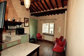 Cozinha com bancada de mármore, pia e janela com vista para edifícios. Há cadeiras vermelhas e um armário verde.