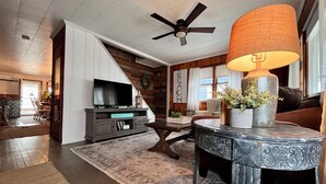 Ein Wohnzimmer mit Fernseher, Deckenventilator, Tisch mit Lampe und Teppich.