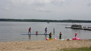 A lake with people on a floating platform, a dock, and inflatable toys on the shore.