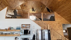 A modern kitchen with wooden ceiling, stainless steel appliances, and a staircase leading to an upper level.