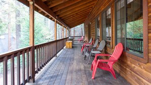 Una terraza de madera con sillas Adirondack rojas y barandilla de madera.