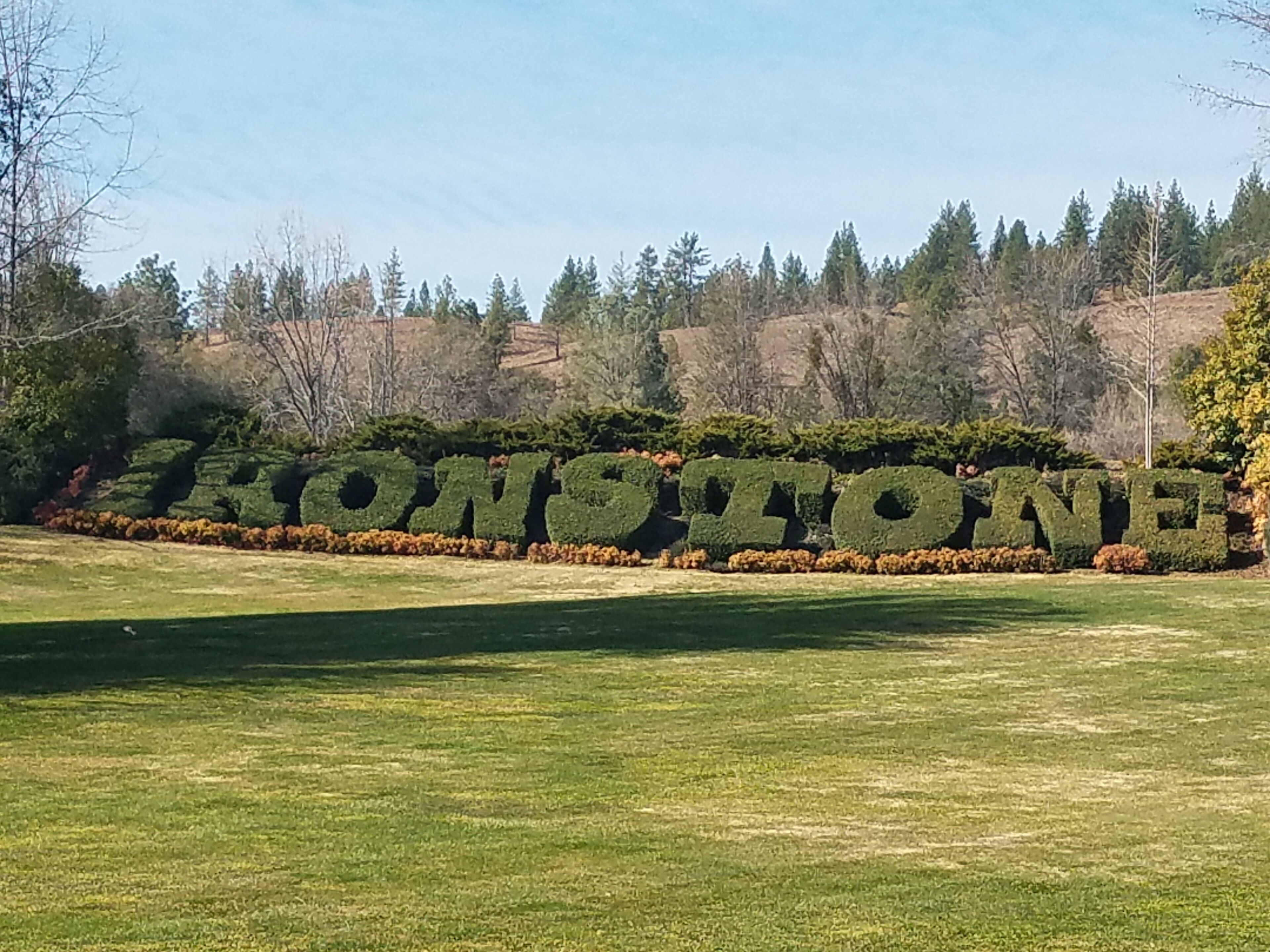 Une pelouse parfaitement entretenue, avec un grand panneau vert, taillé en forme de haie, sur lequel on peut lire le mot « KONSTONE ».