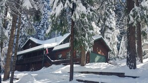 Una cabaña con porche cubierto y garaje, rodeada de árboles cubiertos de nieve.