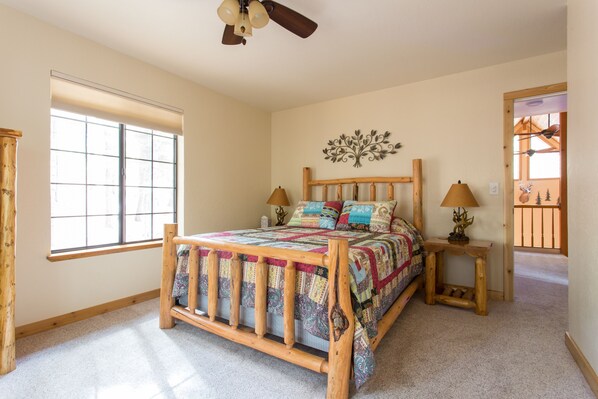 A bedroom with a wooden bed, a window with blinds, a decorative wall piece, and a nightstand with a lamp.