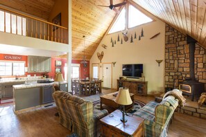 A spacious loft-style living area with a kitchen, dining area, and a stone fireplace.