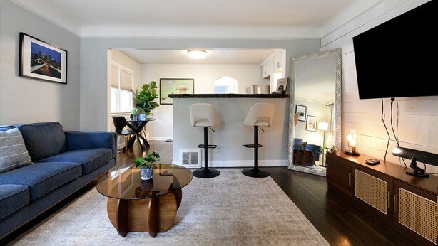 A modern living room with a blue sofa, a glass coffee table, two floor lamps, and a TV on a wooden cabinet.