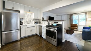 A modern kitchen with stainless steel appliances, white cabinetry, and a wooden floor.