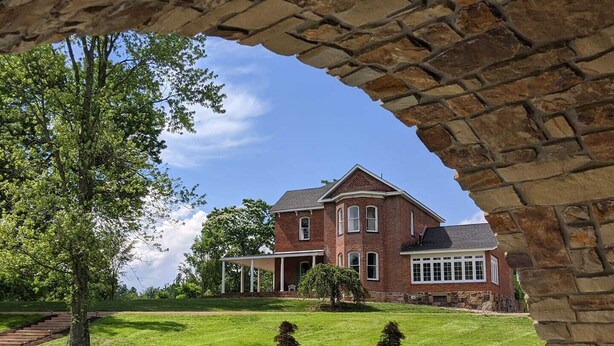 A large brick house with a covered porch, surrounded by a well-maintained lawn and a stone archway. - Historic Home, Modern & Charming Decor, Wine Trail, Private Rental (Alto Pass)
