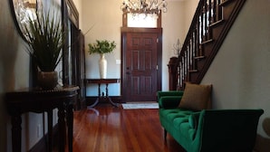 A hallway with a wooden floor, a green sofa, a dark wooden staircase, and a door with a white vase and plant on a small table. - Historic Home, Modern & Charming Decor, Wine Trail, Private Rental (Alto Pass)
