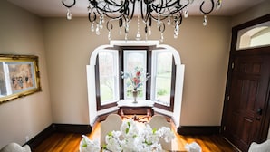 A dining area with a wooden table set for four, a chandelier, and a window with a view of greenery. - Historic Home, Modern & Charming Decor, Wine Trail, Private Rental (Alto Pass)