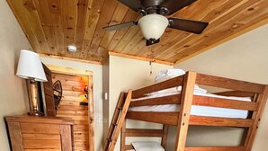 Dormitorio con literas, techo de madera, escritorio con lámpara y ventilador de techo.