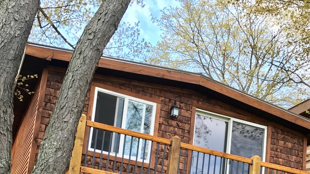 Una cabaña de madera con balcón, una parrilla y mobiliario exterior.