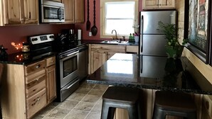 Una cocina con armarios de madera, electrodomésticos de acero inoxidable, encimera de granito y ventana que deja entrar luz natural.