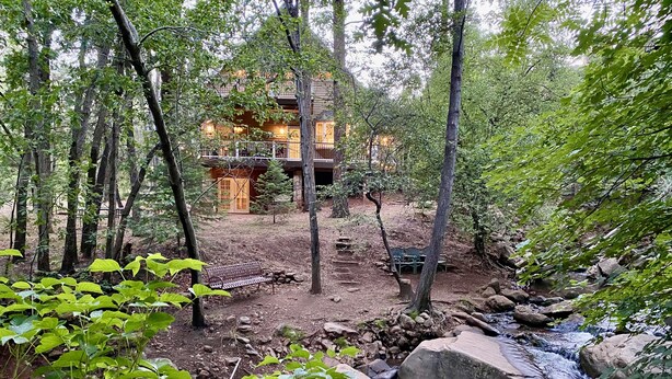 A rustic cabin with a stone exterior, surrounded by dense forest and a small stream. - Riverfront Retreat. Year-round river in North Payson. (Payson)