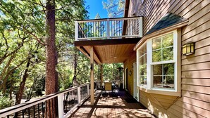 A wooden deck with a railing, a table and chairs, and a window overlooking a forested area. - Riverfront Retreat. Year-round river in North Payson. (Payson)