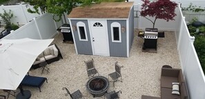 Un patio trasero con un cobertizo pequeño, mobiliario exterior y una zona de barbacoa.