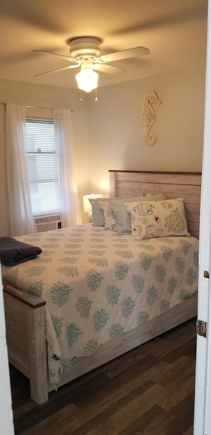 Un dormitorio con cama, ventilador de techo, decoración en la pared y ventana con cortinas.