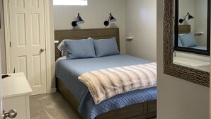 A bedroom with a bed, bedside lamps, a white dresser, a door, and a mirror.