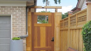 A wooden door with a window, a bench with cushions, and potted plants on a wooden deck.