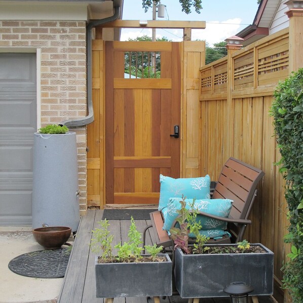 Una puerta de madera con un ventanal, un banco con cojines y plantas en macetas sobre una terraza de madera.