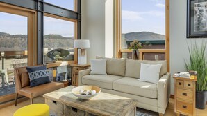 A modern living room with large windows, a beige sofa, a coffee table, and a yellow chair. - UNBEATABLE LOCATION! Downtown Hood River Loft with Views, Pet Friendly (Hood River)