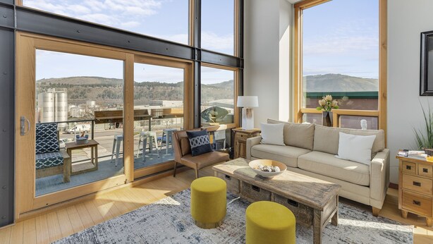 A spacious living area with large windows, a sofa, a coffee table, and a view of the countryside. - UNBEATABLE LOCATION! Downtown Hood River Loft with Views, Pet Friendly (Hood River)
