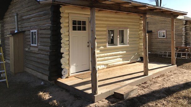 Eine Blockhütte mit Veranda, einer Tür und einem Fenster.