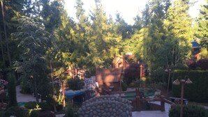 A miniature golf course with a stone bridge over a water feature, surrounded by greenery and a wooden structure in the background. - Starfish Cottage - Oceanside Village Resort (Parksville)
