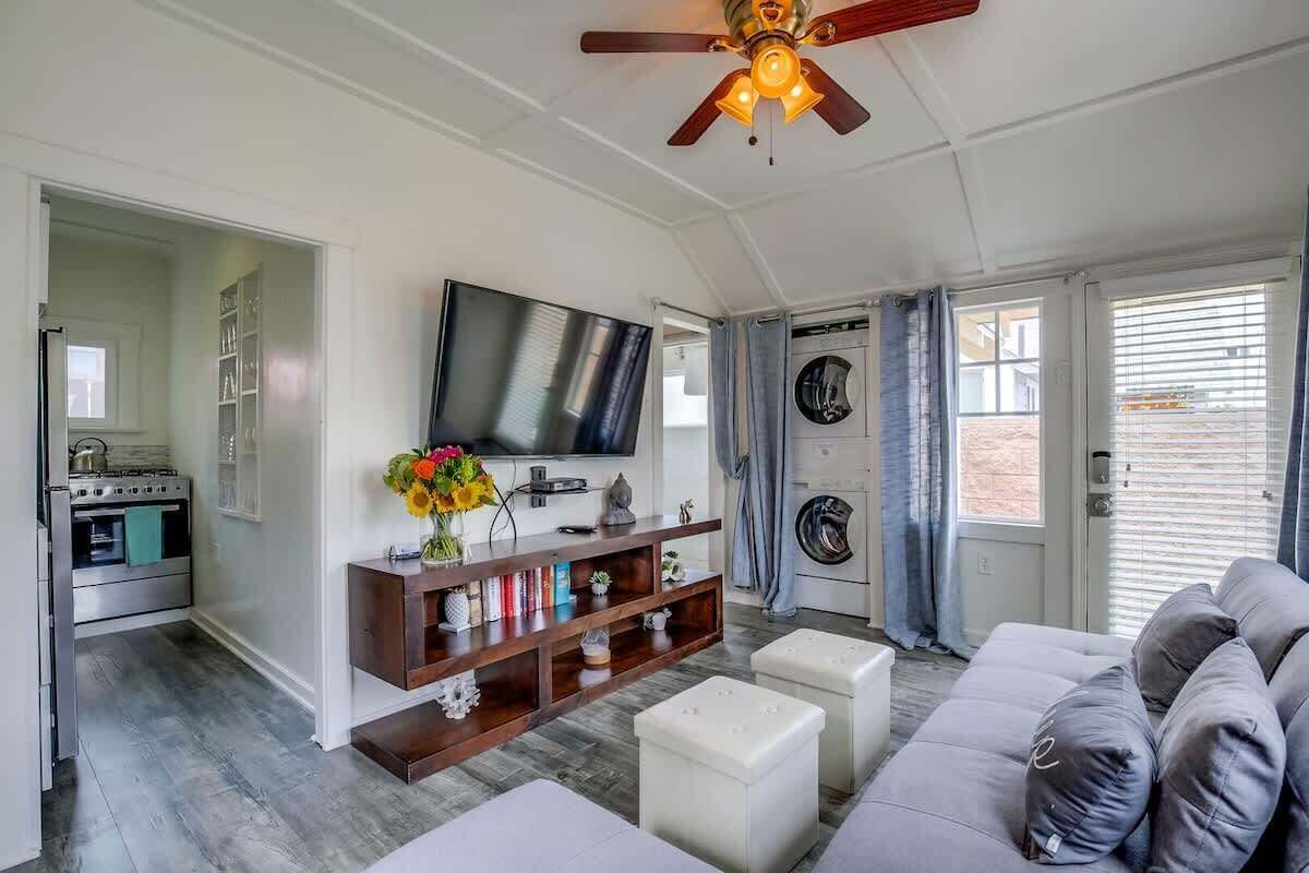 Ett vardagsrum med en TV, ett träinrett mediaskåp, en grå soffa och en takfläkt.