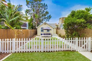 A fenced backyard with a bench, a small house, and a palm tree.