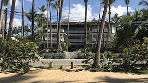 A beachfront hotel with multiple floors, palm trees, and a sandy beach. - Seaside Apartment (Las terrenas)