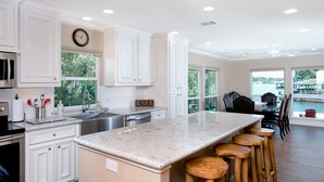 A spacious kitchen with white cabinetry, a large island with stools, and a view of the outdoors through large windows. - A lakefront getaway (Willis)