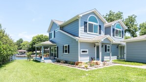 A two-story house with a covered porch, a small front yard with a lawn, and a lake in the background. - A lakefront getaway (Willis)