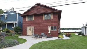 A two-story house with a front porch, a small patio with outdoor furniture, and a well-maintained lawn. - Eagle Lake Kalamazoo, Mattawan - Lake Livin' (Mattawan)