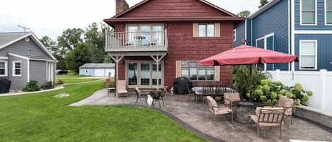 A two-story house with a patio area featuring outdoor furniture, a grill, and a red umbrella.