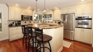 A kitchen with white cabinets, stainless steel appliances, and a central island with bar stools. - Eagle Lake Kalamazoo, Mattawan - Lake Livin' (Mattawan)