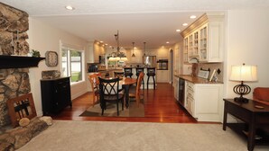 A spacious kitchen with white cabinets, a dining area with wooden chairs, and a stone fireplace. - Eagle Lake Kalamazoo, Mattawan - Lake Livin' (Mattawan)