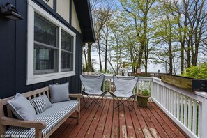 Une terrasse en bois avec un banc et deux chaises, donnant sur une étendue d’eau et des arbres.