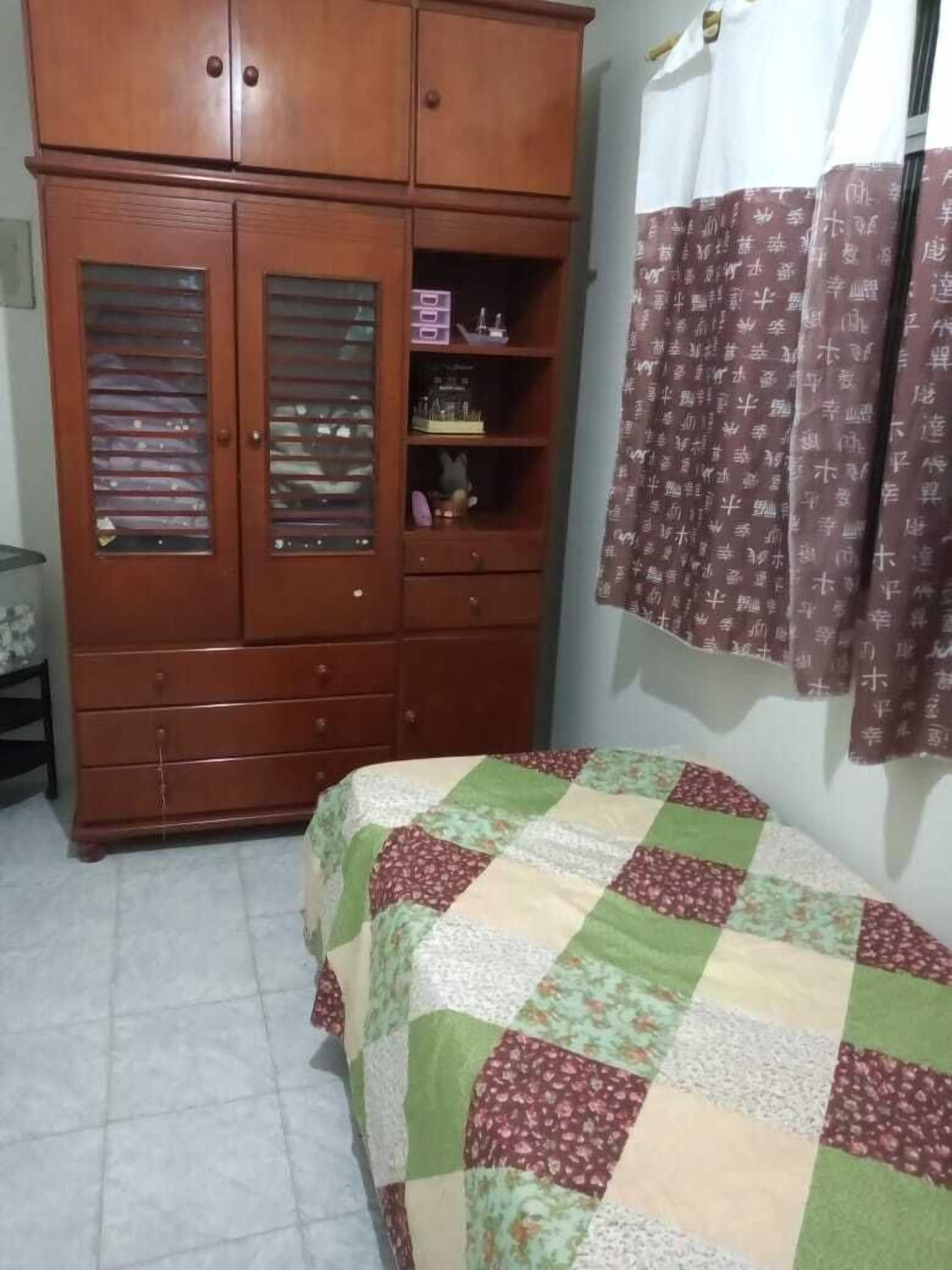 Une chambre avec une armoire en bois, un lit recouvert d’une courtepointe et un rideau à motifs.
