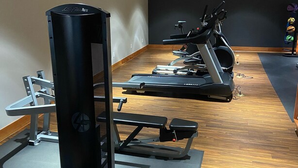 A gym with exercise equipment including a weight machine, treadmills, and a bench.