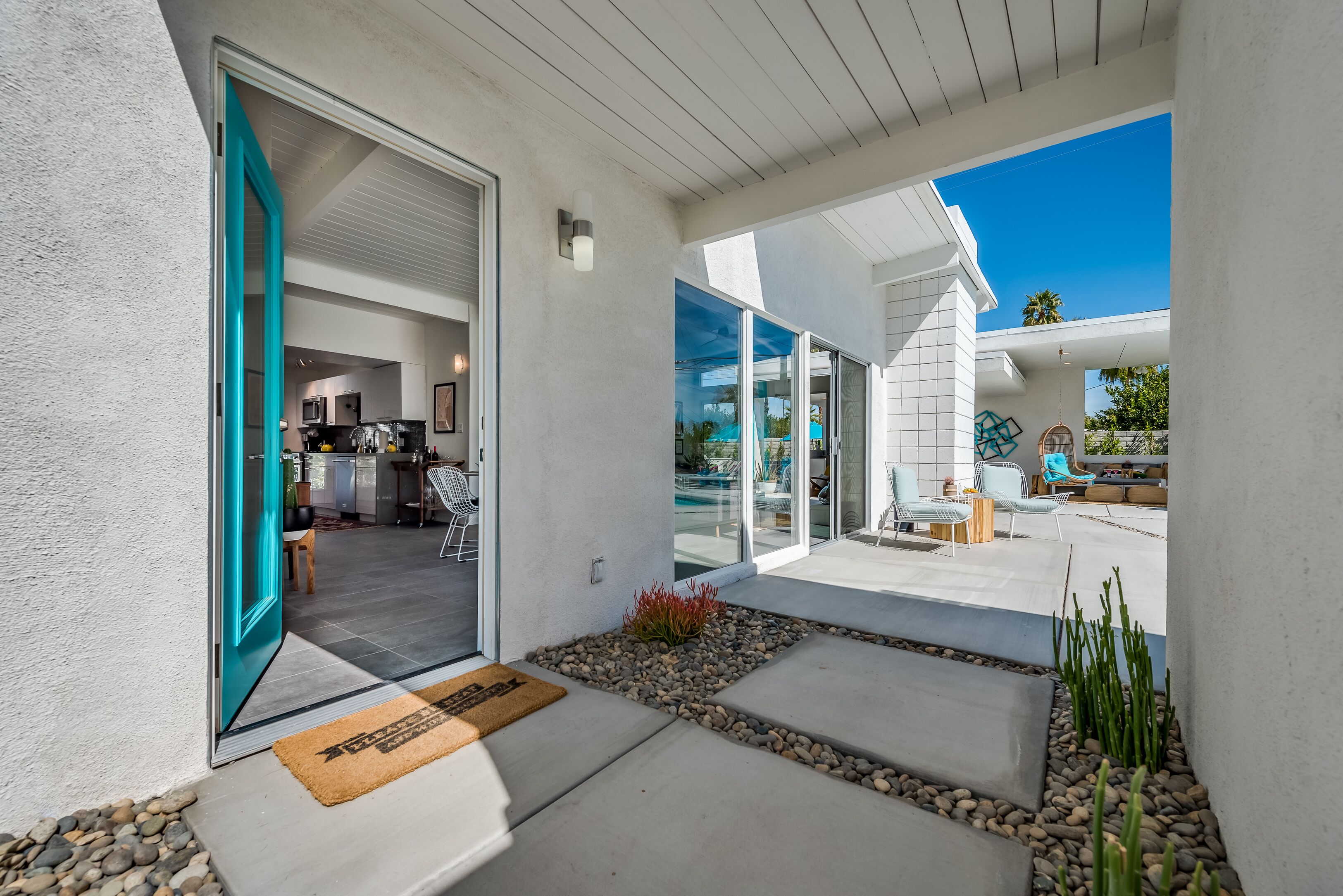 A modern house with a patio, a door leading to a kitchen, and a pool area visible through glass doors.